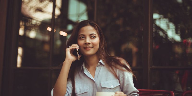Lady at table with cup and smiling with mobile phone to ear